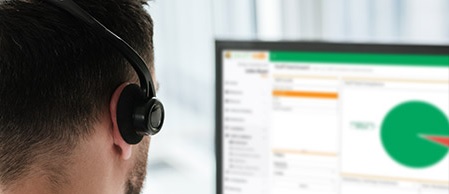 A man, viewed from behind, wears a headset while looking at a computer screen displaying charts and data.